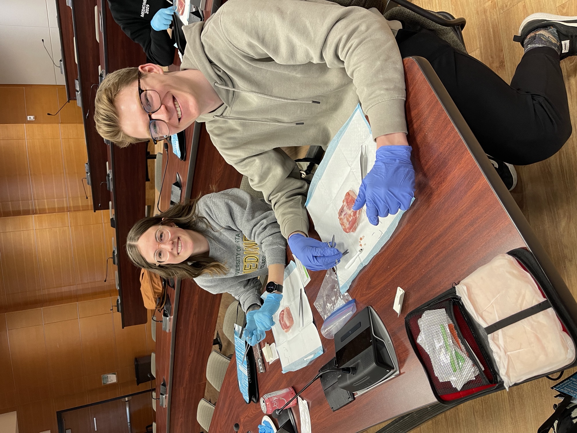 Two medical trainees practising procedural skills with instruments and tissue models at a SkinCourses workshop